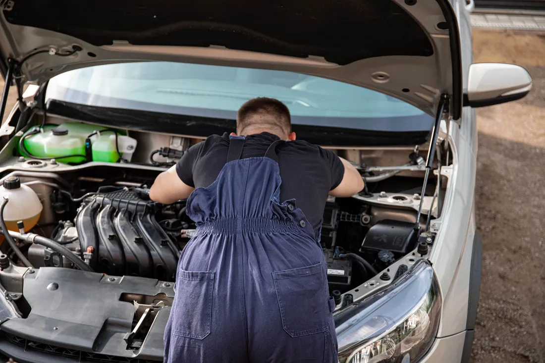 Illustrative mechanic working under an open vehicle hood
